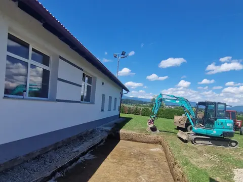 Bager Kobelco izkopava jarek ob stavbi
